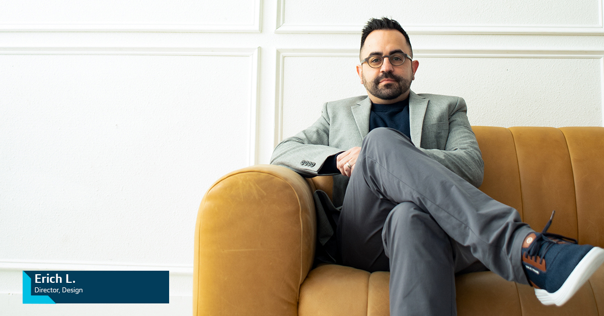 Erich L., Capital One Design Director, sits on a tan couch with his leg crossed